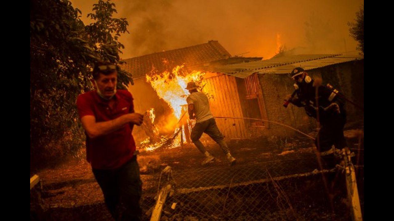 A firefighter and locals rush to a burning house in an attempt to extinguish forest fires.